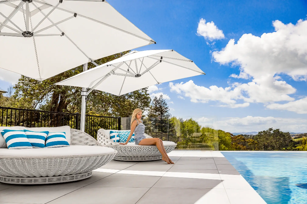 Luxury resort pool deck featuring oversized woven daybeds and large white Frankford cantilever umbrellas overlooking an infinity pool.